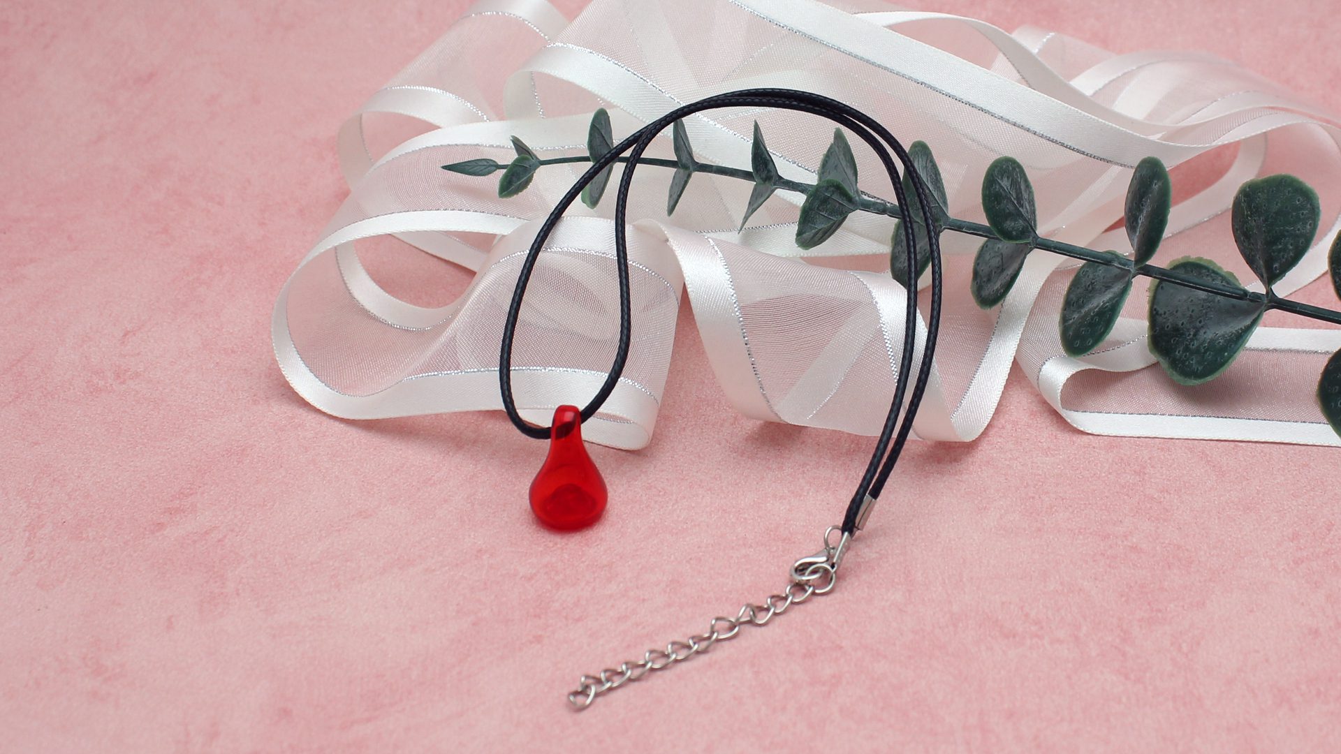 Pendentif olfactif rouge transparent monté sur un cordon noir réglable de 44 à 49 cm.