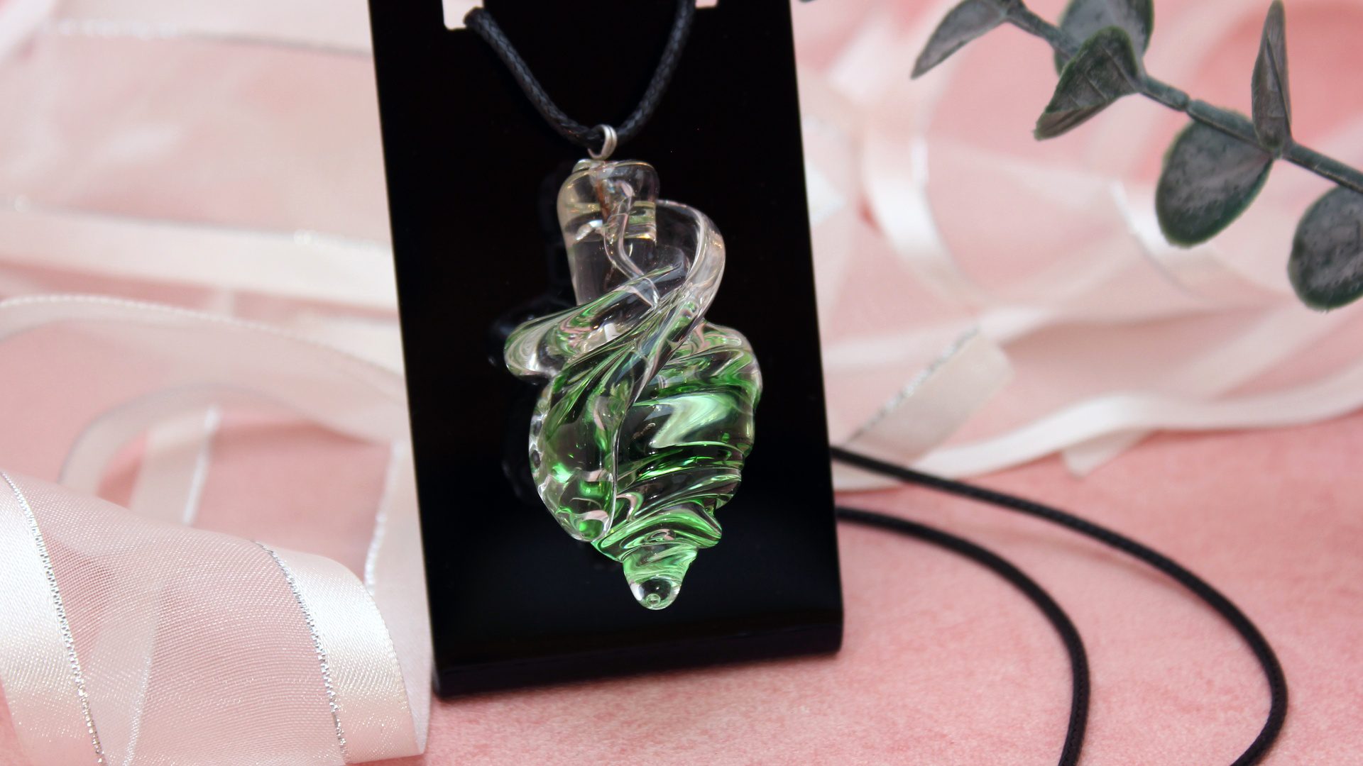 Collier pendentif torsadé vert et transparent en verre recyclé présenté sur support noir